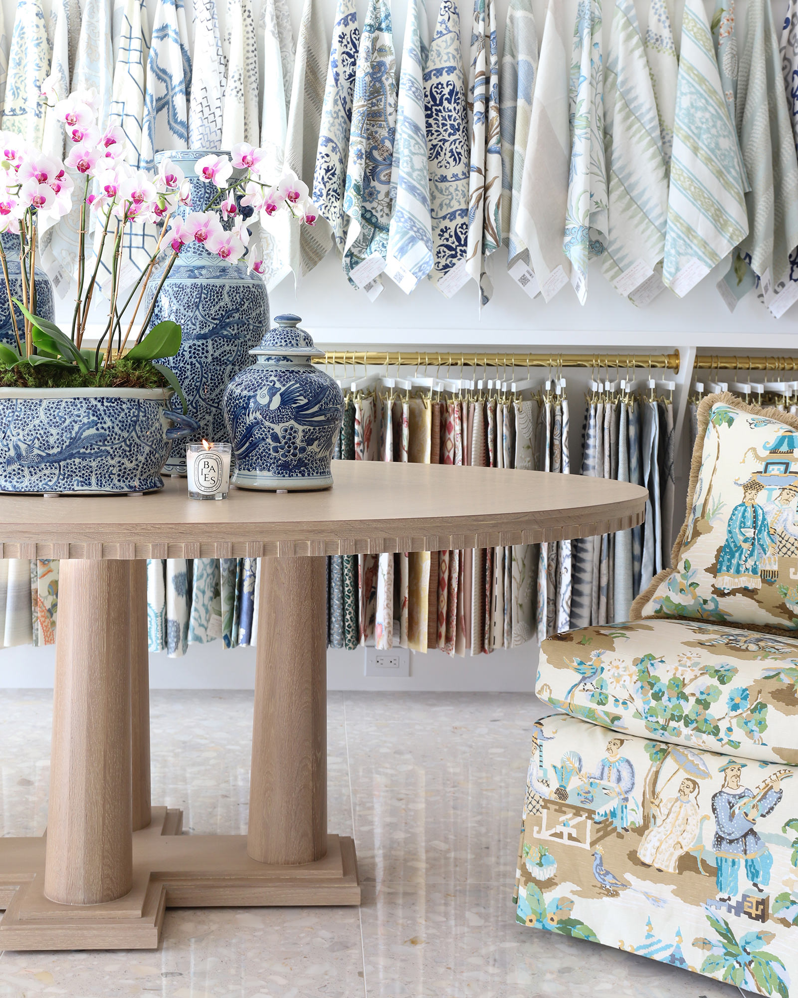 image of showroom fabric room with hanging fabrics on wall ad round center table decorated with blue and white ginger jars and an upholstered chair