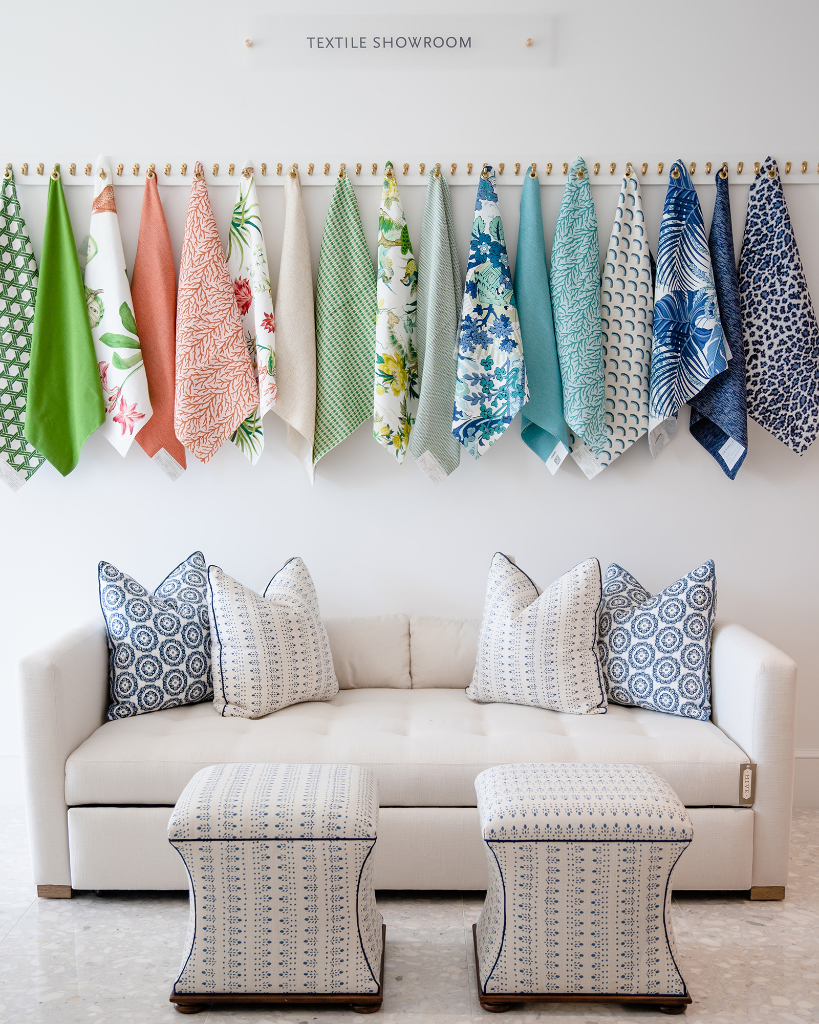 Image of showroom fabric wall with white sofa and blue and white pillows underneath