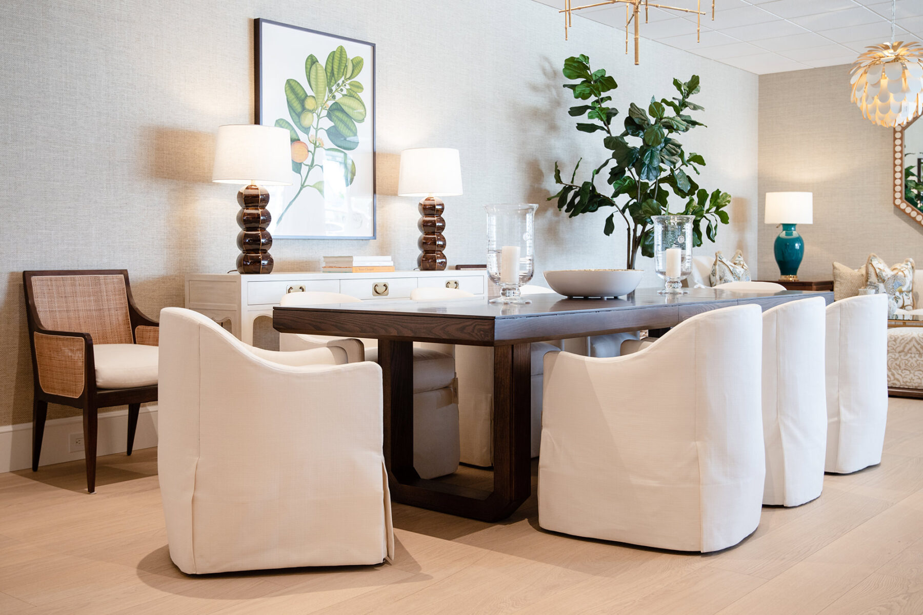 elegant dining space with rich walnut dining table and white upholstered dining chairs, green botanical print on a the wall above a cream buffet with brown table lamps