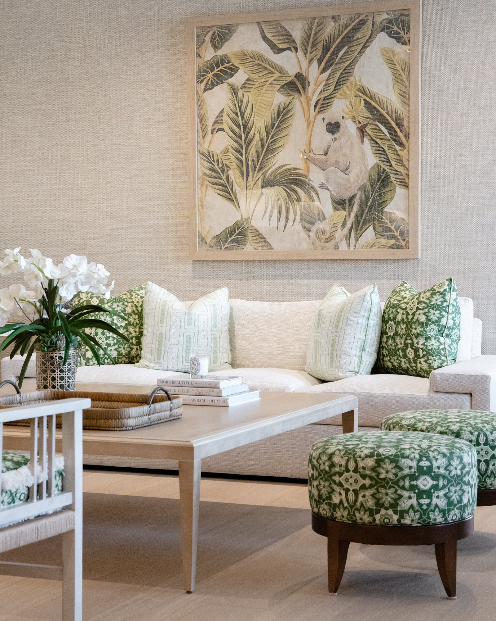 image of showroom living space with neutral white and beige tones with pops of green patterned pillow and stool and featuring a tropical palm print with a monkey