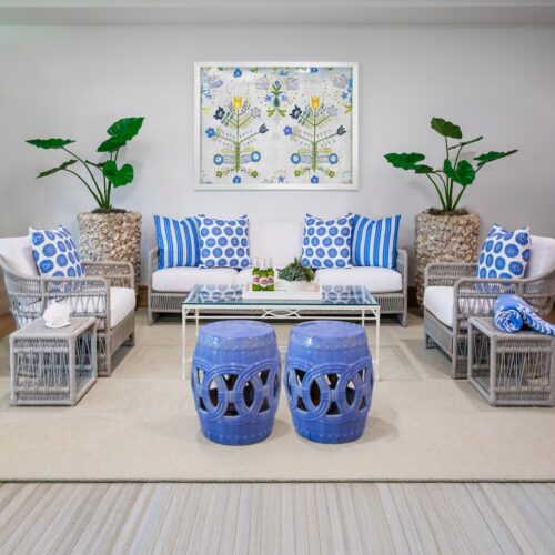 outdoor furniture grouping of gray woven chairs and sofa with white cushions and blue pillows, with 2 blue garden stools